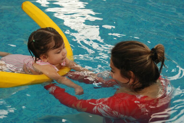 Frau begleitet ein kleines Kind mit Schwimmnudel im Schwimmbecken