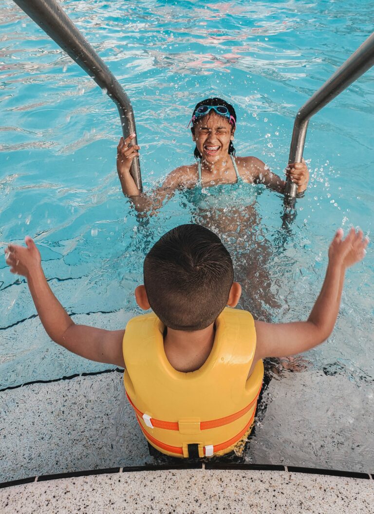 Kind mit Schwimmweste steigt über die Leiter ins Becken